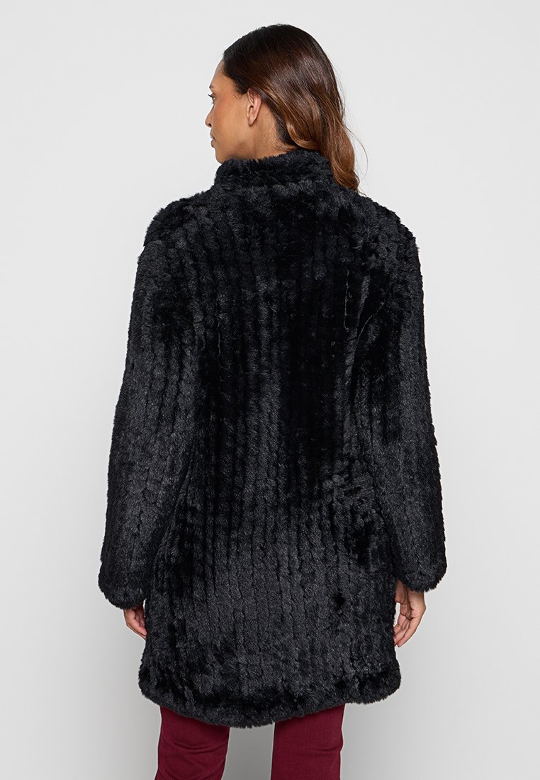 Fekete műszőrme kabát bordázott textúrával. Magas gallérral és hosszú ujjakkal rendelkezik, középhosszúságú, a comb közepéig ér.