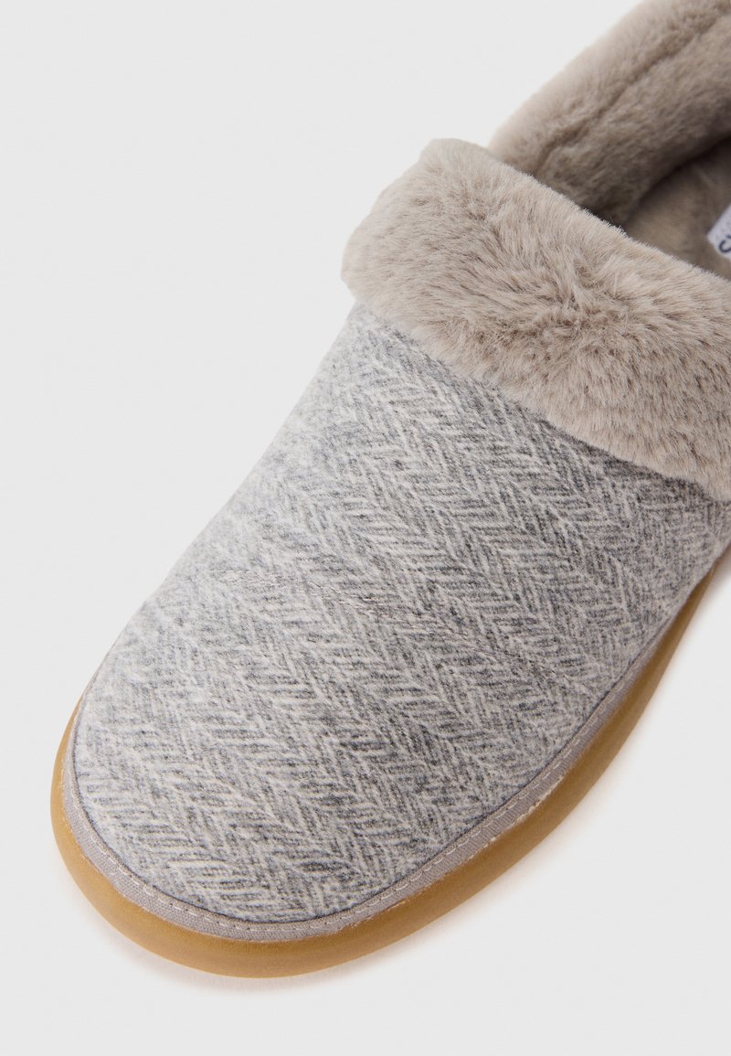 Szare wełniane kapcie z wzorem w jodełkę, miękka beżowa futrzana mankieta oraz jasnobrązowa gumowa podeszwa. Okrągły kształt palców.