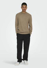 Lysebrun langærmet sweater parret med sorte bukser og hvide sneakers. Sweateren har en rund halsudskæring og ribbede manchetter.
