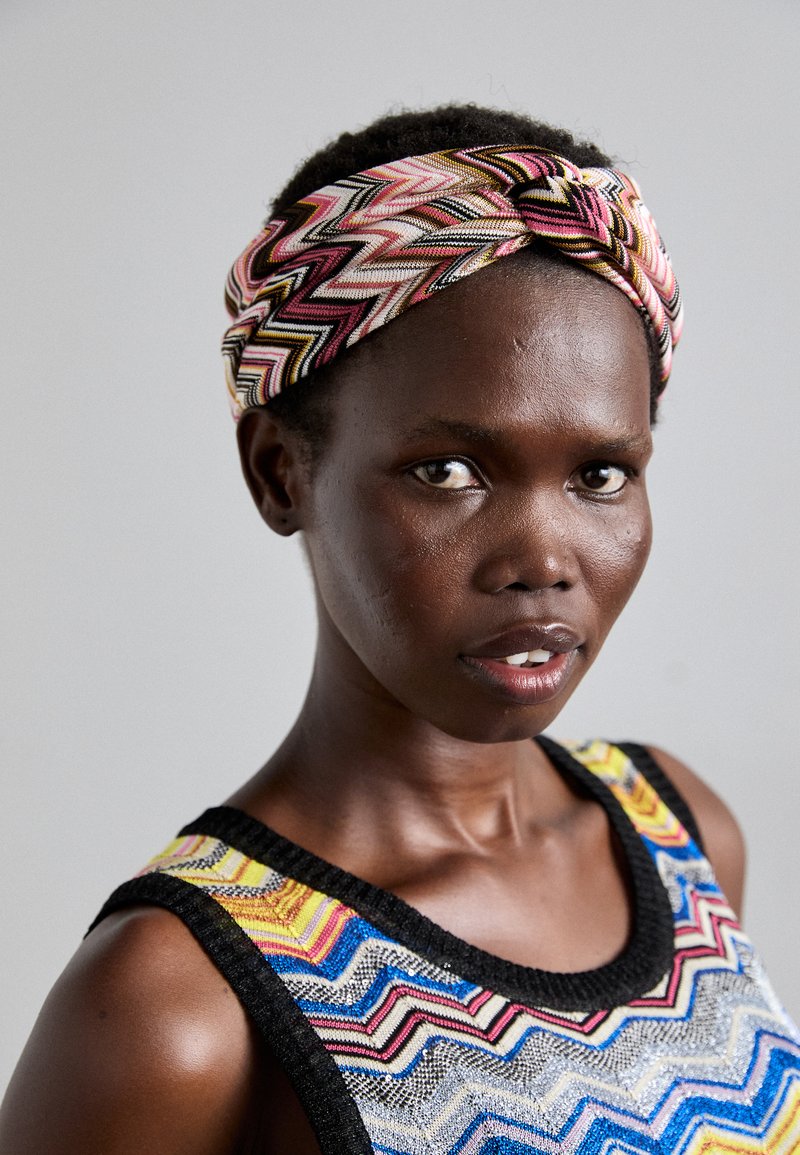 Bandeau tressé en rose, noir et motif zigzag jaune. Haut sans manches multicolore avec un design géométrique et un tissu texturé.