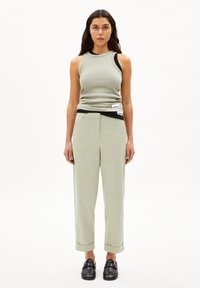Hellgrünes, geripptes Tanktop und hellgrüne Hose mit aufgerolltem Saum. Schwarze Slipper. Einfaches Design, minimale Details.