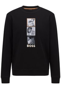 Sudadera negra con un gráfico central de tres fotos en blanco y negro y la palabra "BOSS" en letras blancas en negrita.