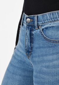 Jeans de mezclilla azul claro con un botón a presión plateado, presillas para el cinturón y diseño de cinco bolsillos con una sutil textura desgastada.