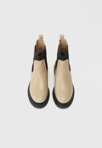 Bottes en cuir beige à cheville avec des panneaux latéraux élastiques noirs, bout rond, surface texturée et semelles en caoutchouc. Aucun matériel ou motif visible.