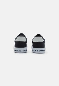 Tmavě modré plátěné tenisky s bílou gumovou podrážkou a polstrovanými šedými akcenty na patě. Na zadní straně je vytištěno "JACK & JONES".