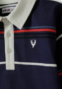 Granatowa koszulka polo z jasnoszarym kołnierzykiem; features poziome paski w kolorach czerwonym, niebieskim i białym; posiada wyhaftowane logo jelenia oraz zapięcie na guziki.