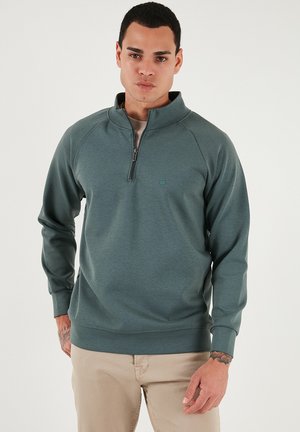 Dunkelgrüner Pullover mit Viertelreißverschluss aus weichem Stoff, mit Raglanärmeln und kleinem Logo auf der Brust. Gestrickte Bündchen und Saum.