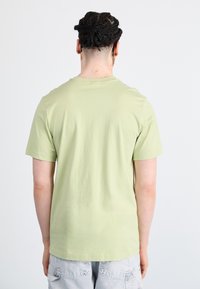 Βαμβακερό μπλούζα κοντομάνικη, ανοιχτό πράσινο, με στρογγυλή λαιμόκοψη, εμφανίζεται από πίσω, δείχνοντας μια λεία υφή και απλό σχέδιο.