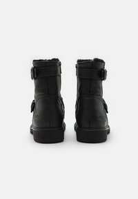 Schwarze Lederstiefeletten mit strukturiertem Finish, seitlichem Schnallen-Detail und Kunstfell-Futter an der Oberseite und Ferse. Flache schwarze Sohle.
