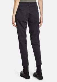 Black, fitted pants with a smooth texture, two back pockets, and a straight leg cut. Paired with black ankle boots.