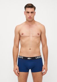 Temno modri boksarji iz bombaža, s črnim pasom z logotipom Lacoste. Oblika je krojena s kratkimi hlačnicami.