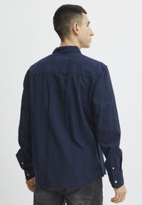 Camicetta a maniche lunghe blu navy realizzata in tessuto strutturato, con colletto abbotttonato e bottoni ai polsini, dalla linea dritta e fessure laterali.