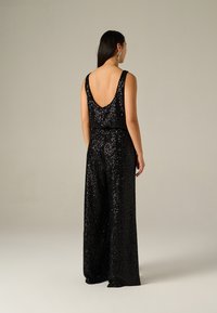 Jumpsuit noir en sequins avec un dos en V plongeant, une coupe évasée et des bretelles larges, mettant en valeur une texture lisse et réfléchissante ainsi qu'une drape élégante.