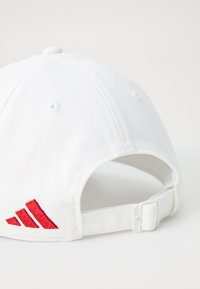 Hvid baseballcap med rødt Adidas-logo på siden og justerbar rem med spænde bagpå på en ensfarvet lys baggrund.