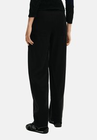 Pantalones negros de pierna ancha hechos de tela suave, con dos bolsillos traseros y cintura elástica. Combinados con zapatos negros sin cordones.