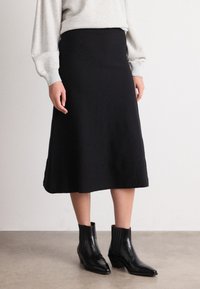 Zwarte A-lijn midi-rok van een gladde stof, met een getailleerde tailleband en zijinsnijdingen, gecombineerd met elegante zwarte enkellaarsjes.
