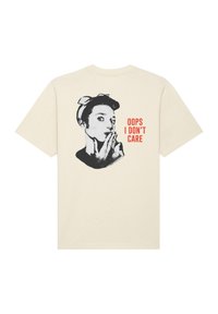 Béžové bavlněné tričko s grafikou ženy s tmavými vlasy a mašlí, pod níž je červený text "OUPS, NESTARÁM SE".