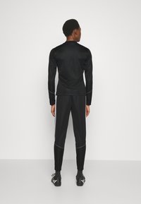 Čierny športový top s dlhými rukávmi a okrúhlym výstrihom, skombinovaný s čiernymi nohavicami so bočnými bielymi pruhmi. Hladká textúra, priliehavý strih.