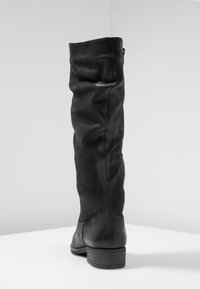 Botte haute jusqu'au genou en cuir noir avec une coupe décontractée. Caractérisée par un bout arrondi et un talon bas empilé. La surface texturée présente de légères plis.