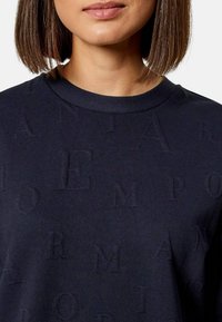 Felpa navy con texture in rilievo che presenta le lettere "Emporio Armani". Collo tondo e texture in tessuto morbido, vista cropped del petto.