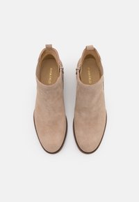 Stivaletti alla caviglia in suede beige con una texture liscia, punta arrotondata, chiusura con zip laterale e suola in un marrone chiaro a contrasto.