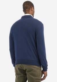 Mörkblå stickad tröja med rund halsringning, ribbad i ärmslut och nederkant, samt en slät textur. Har en baksida utan synliga logotyper.