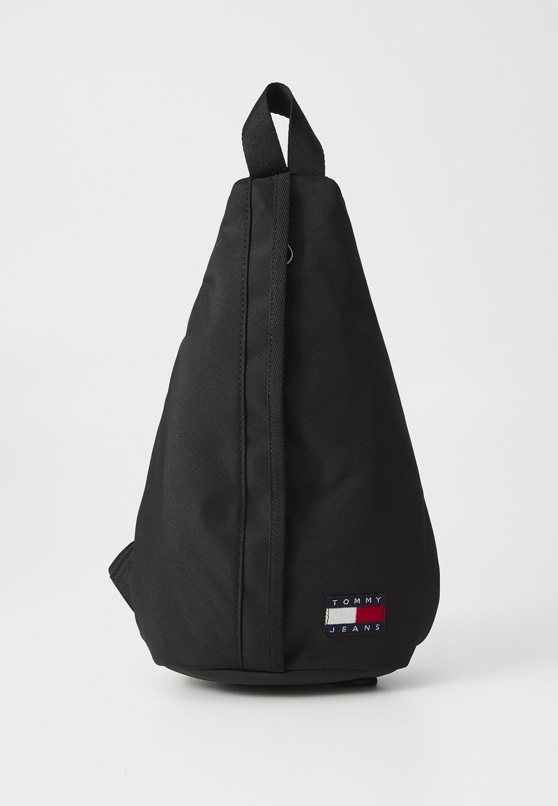 Sort stof sling tas med en triangel-form, der har et håndtag på toppen, en lynlås på siden og et lille mærke med logo.