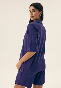Fioletowa koszulka polo z krótkim rękawem i luźnym krojem, w zestawie z dopasowanymi szortami. Wykonana z teksturowanej tkaniny, z subtelnym logo.