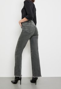 Jeans de denim gris de tiro alto con pierna recta, dobladillo deshilachado y dos bolsillos traseros, combinados con zapatos de tacón alto negros.