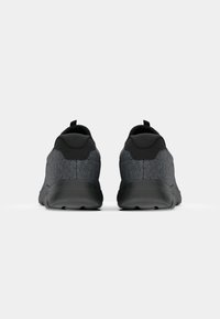 Paire de chaussures de sport gris foncé avec semelles et languettes de talon noires, vues de dos sur un fond gris clair.
