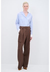 Hellblau gestreifte Button-up-Bluse mit einer Tasche, kombiniert mit hoch taillierten, braunen weit geschnittenen Hosen im Cargo-Stil mit seitlichen Taschen.