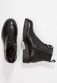 Svarta läderankelboots med rund tå, snörning framtill, sidodragkedja och robusta sulor. Slät yta med minimala metallaccent.