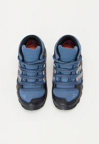 Blue mesh sneakers with black rubber soles, featuring gray accents and lace-up design. Interior has red padding. Textured surface with patterned details.
