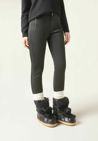 Svarta faux-läderbyxor med två dragkedjefickor, slim fit, tillsammans med svarta stövlar med pälsfoder och vita stickade manschetter.