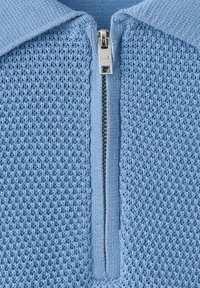 Prenda de punto azul claro por delante mostrando cremallera metálica plateada con tirador y patrón texturizado en relieve en la tela.
