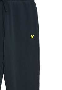 Mörkblå träningar med dragkedja i midjan, med en liten gul broderad logotyp på vänster ben. Mjuk bomullsblandning.