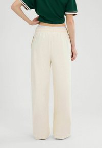 Crème kleurige wijde broek van zacht materiaal, met een elastische tailleband en zijzakken. Geen zichtbare patronen of hardwaredetails.