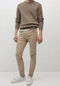 Beżowy sweter w prążki, jasnobeżowe dopasowane spodnie oraz białe trampki. Prosty design z delikatną fakturą; bez wyraźnych wzorów ani ozdób.