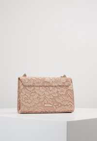 Borsa a tracolla rosa in pizzo con design strutturato, caratterizzata da un accento in metallo dorato e una chiusura a pattina. Motivo floreale testurizzato su tutta la superficie.