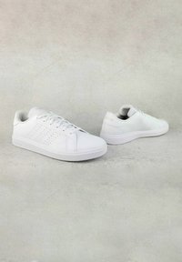 Pair of white low-top Adidas sneakers with laces and perforated stripes on a light textured background.