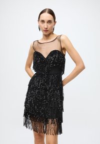 Black dress with a fitted bodice, sheer neckline, and fringed sequins cascading to the hem. Features a smooth texture with a layered design.