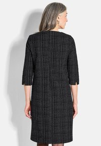 Robe noire avec un motif texturé, manches trois-quarts et fente légère à l'ourlet. Présente une coupe droite et des détails de couture au dos.