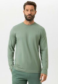 T-shirt à manches longues et col rond en tissu vert clair. Texture douce avec une coupe décontractée, associé à un pantalon de sport vert assorti.