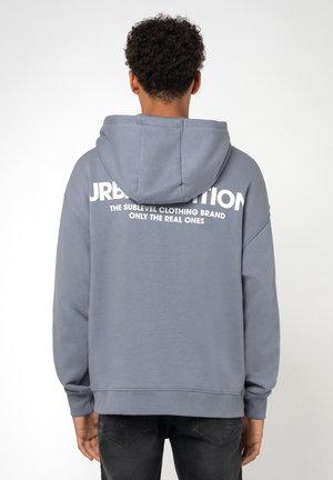 Graue Kapuzenjacke mit einer Kapuze, die auf der Rückseite großen weißen Text trägt. Hergestellt aus weichem Stoff, mit gerippten Bündchen und Saum. Lässige Passform und Design.