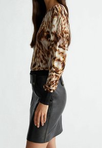 Maglietta a maniche lunghe con stampa animale marrone e crema, abbinata a una mini gonna in pelle nera caratterizzata da una texture liscia e due tasche.