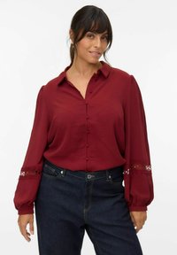 Bordeaux knoopblouse met pofmouwen, kantaccenten bij de manchetten en een textuurstof, gecombineerd met een donkere denim high-waisted jeans.
