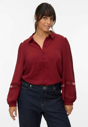 Burgundy button-up blouse with puff sleeves, lace accents at cuffs, and textured fabric paired with dark denim high-waisted jeans.