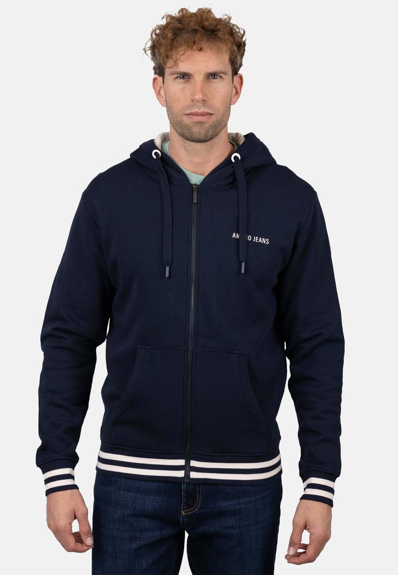 Sudadera con capucha azul marino con cremallera, capucha con cordón, dos bolsillos delanteros y puños y dobladillo acanalados con rayas blancas. Cuenta con el logo "AMMO JEANS" en el pecho.