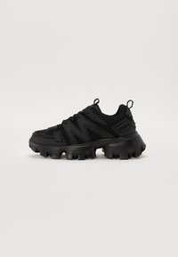Sneaker noire avec une tige en maille texturée, une semelle épaisse et un système de laçage unique. Capte des accents en caoutchouc courbés et une languette en boucle.