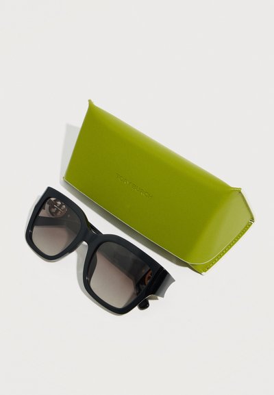 Μαύρα υπερμεγέθη γυαλιά ηλίου με τετράγωνο σχήμα και φακούς με διαβάθμιση, δίπλα σε θήκη από δέρμα σε ελιά πράσινο χρώμα με ανάγλυφο λογότυπο.